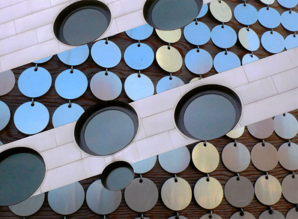Rows of metal disks meet cut-out stripes of building with round windows.